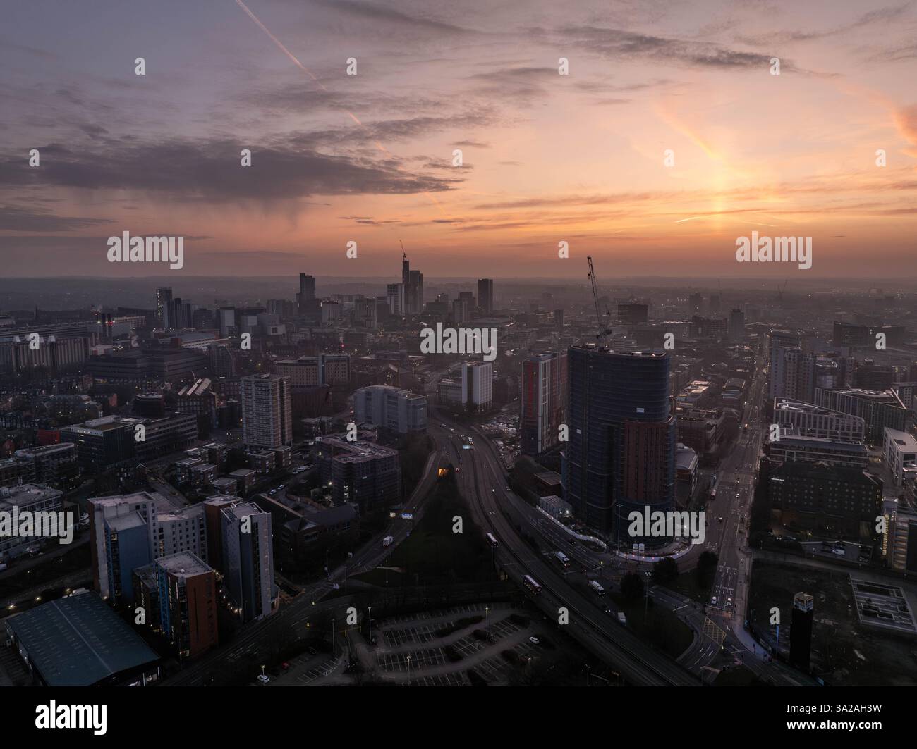 A captivating aerial view showcases Leeds city centre during dawn with beautiful golden hour lighting. The urban skyline and cityscape highlight ongoi Stock Photo