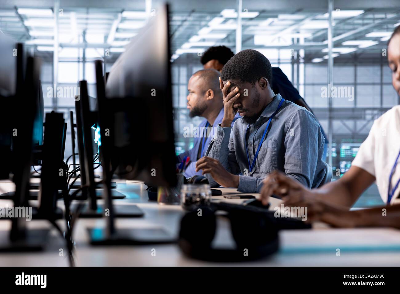 Tired engineer feeling headache while reconfiguring server farm to optimize it for data processing requirements. Stressed man working overtime to ensure data center gear operates efficiently Stock Photo