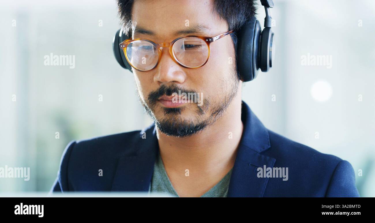 Developer, headphones or man with glasses in office for technology, podcast playlist or coding. Face, music and Asian programmer on computer with Stock Photo