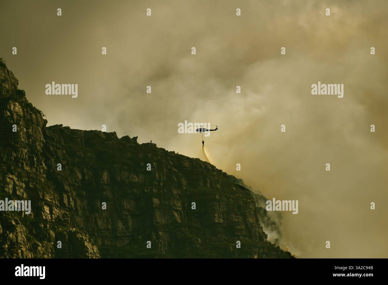 Yellow emergency helicopter carrying a water bucket to extinguish a bush fire. Table Mountain National Park, Cape Town South Africa Stock Photo