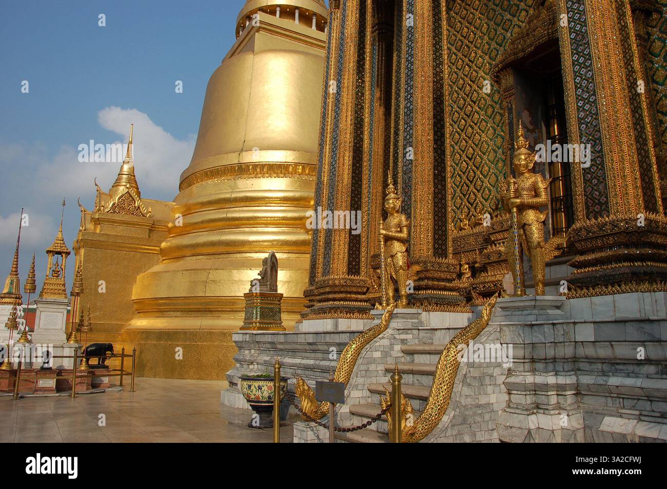 Golden guardian statues stand before the intricately decorated entrance of Phra Mondop at Bangkok’s Grand Palace, showcasing Thai craftsmanship Stock Photo