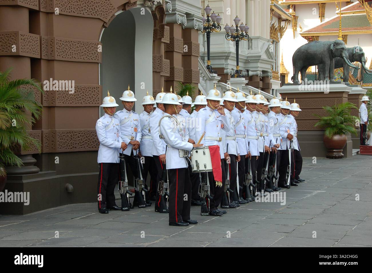 Royal Thai guards in elegant white uniforms and helmets stand in formation at the Grand Palace in Bangkok during a ceremonial duty Stock Photo