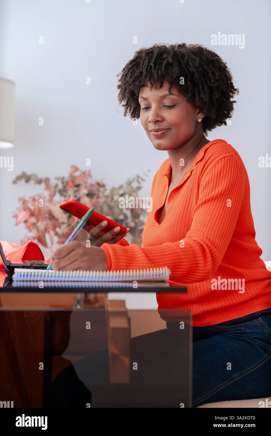 African American student using smartphone while studying at home with laptop Stock Photo