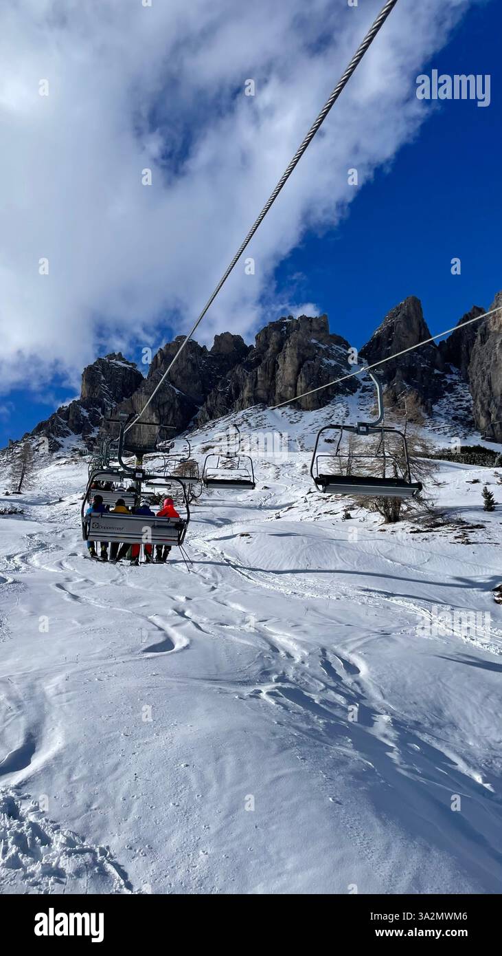 Skiers sitting in a chairlift up a snowy beautiful mountain slope with rugged  peaks in the background on a sunny winter day in the Alps - Smartphone Captured Stock Image