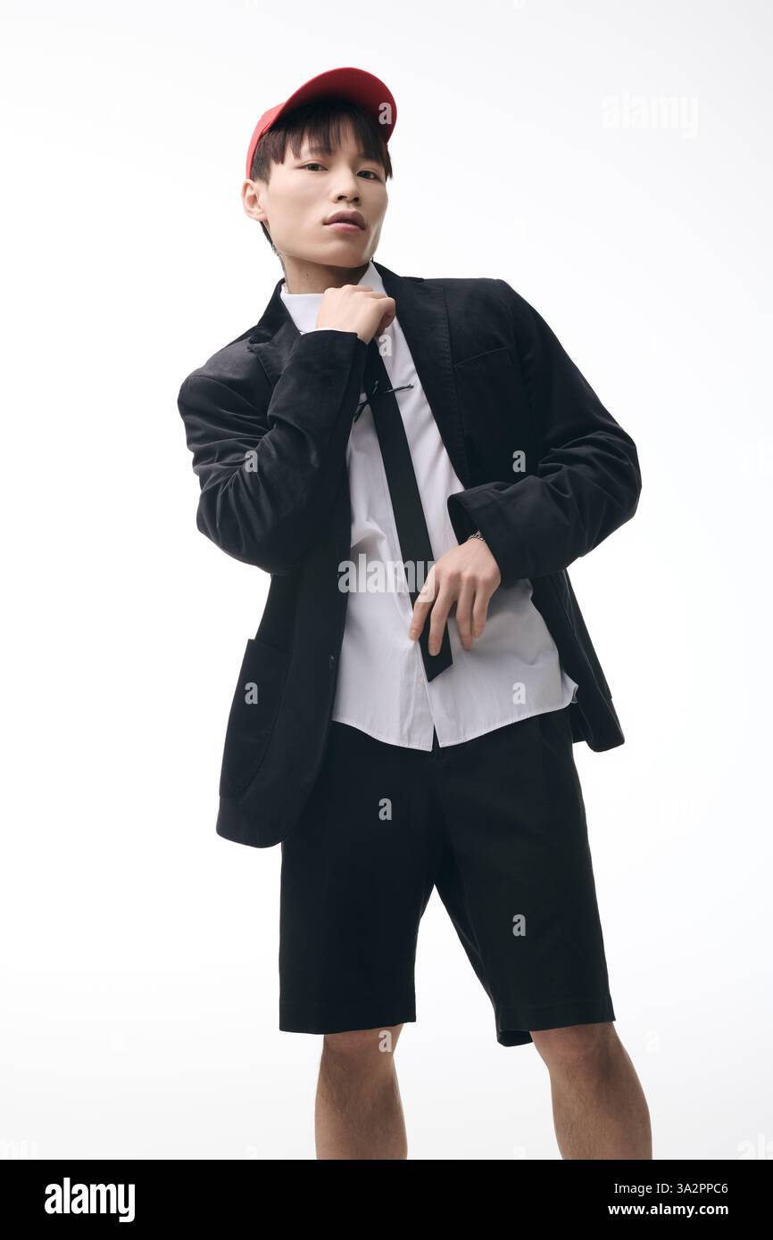 Stylish young Asian man adjusts his tie and jacket with a playful ...