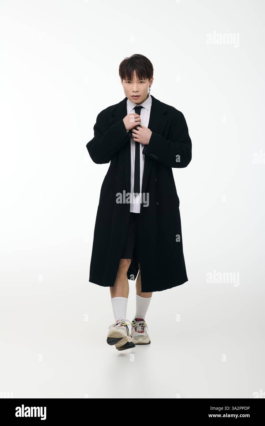 A handsome young Asian man in stylish attire adjusts his tie with ...