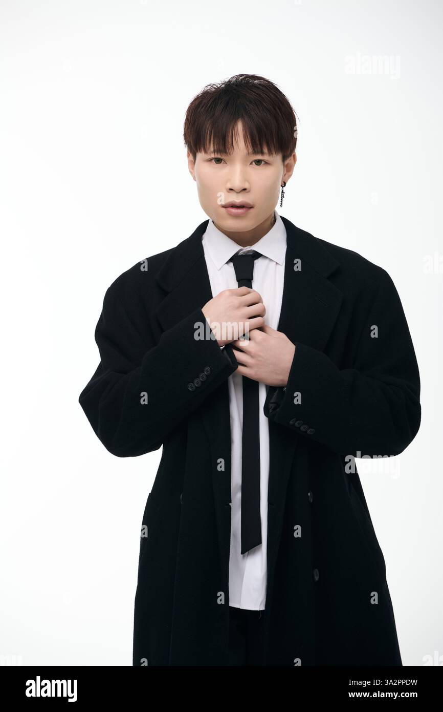 A well groomed young Asian man confidently adjusts his tie in a stylish ...