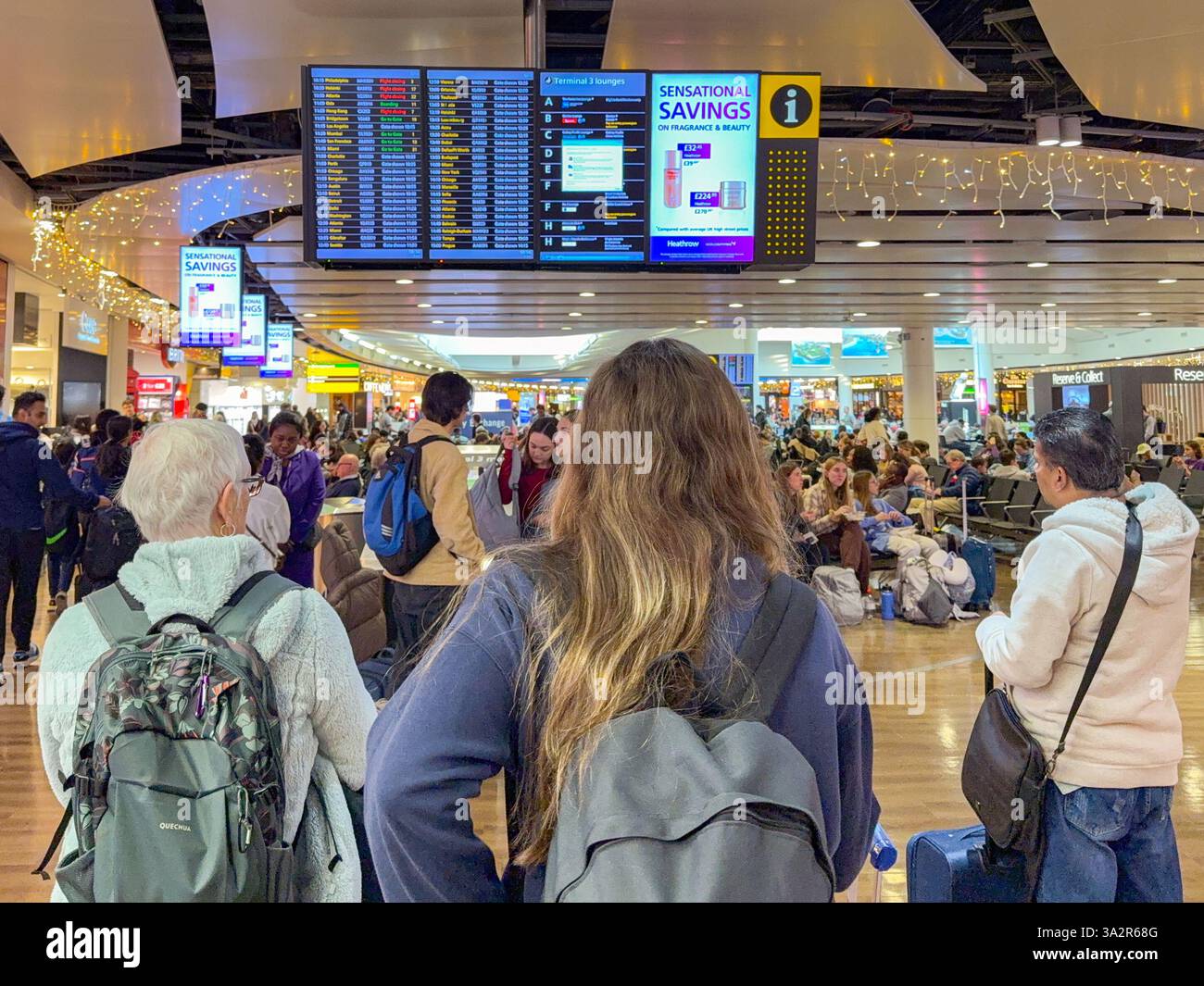 London, England, UK - 3 January 2025: Passengers checking flights on a departures board display screen in Terminal 3 at London Heathrow Airport - Smartphone Captured Stock Image