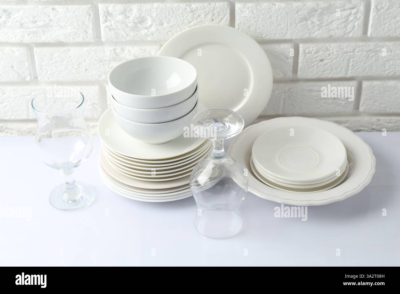 Different clean dishware on white table near brick wall Stock Photo