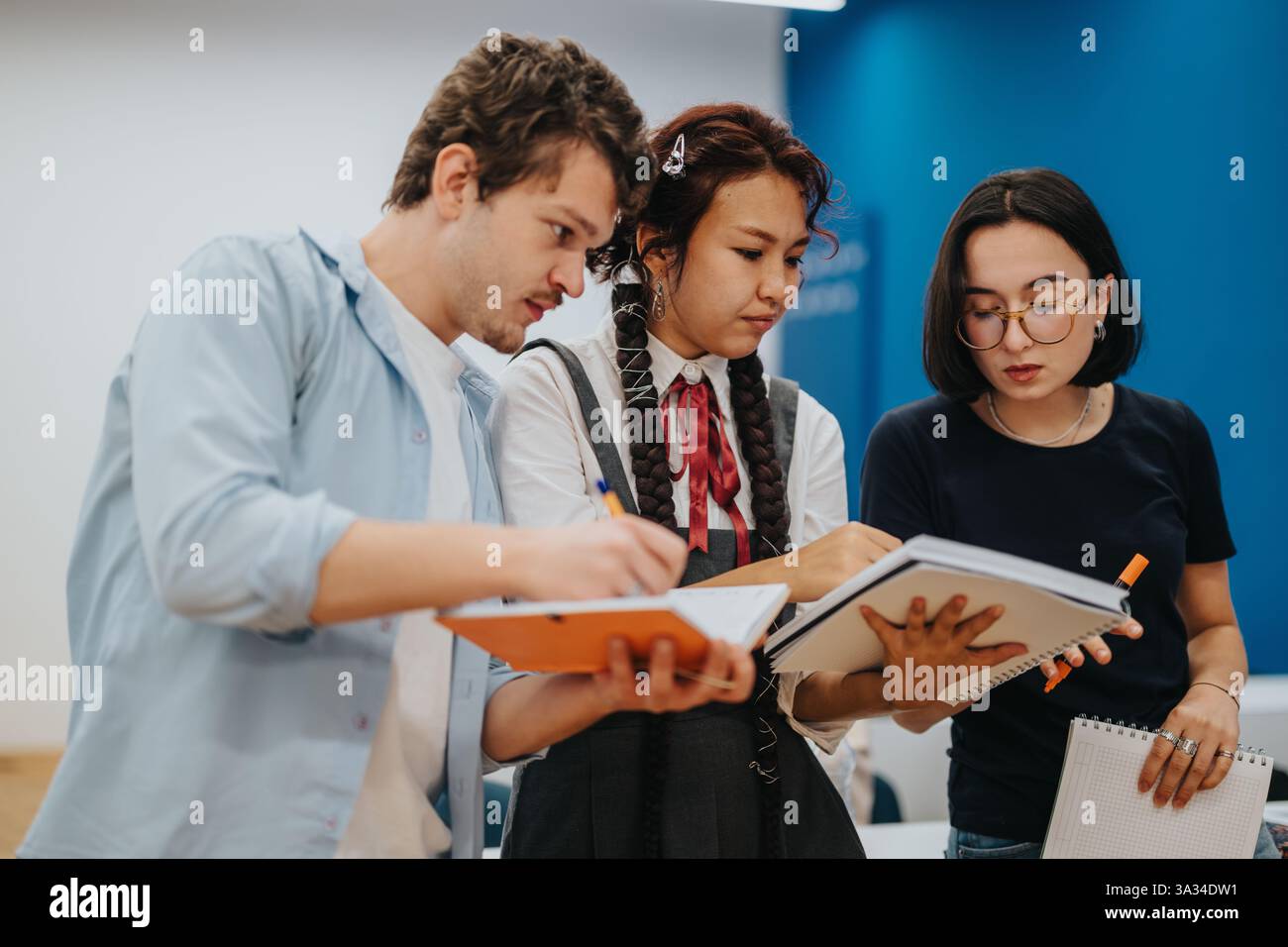 Three students collaborating on a group project in a classroom Stock Photo