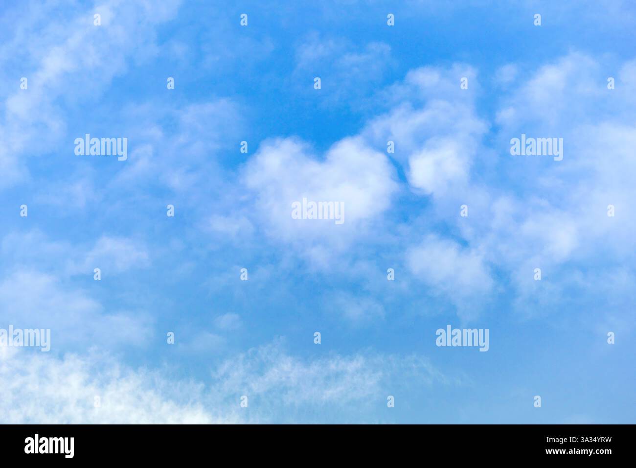 A beautiful heart-shaped cloud floats in a bright blue sky, creating a dreamy and romantic scene. The soft, fluffy texture of the clouds enhances the Stock Photo