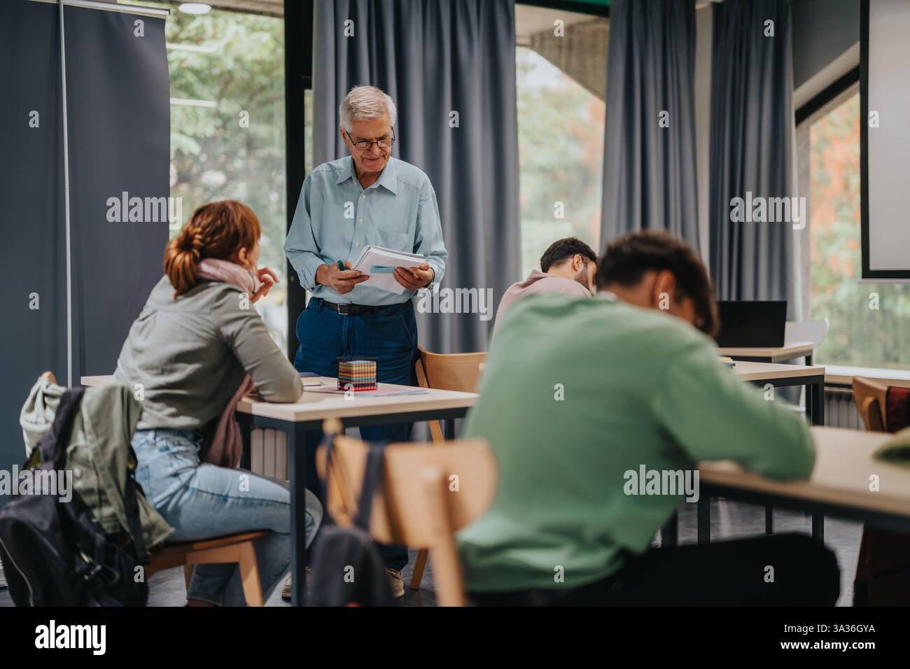 Elderly professor engaging with attentive students in classroom setting Stock Photo