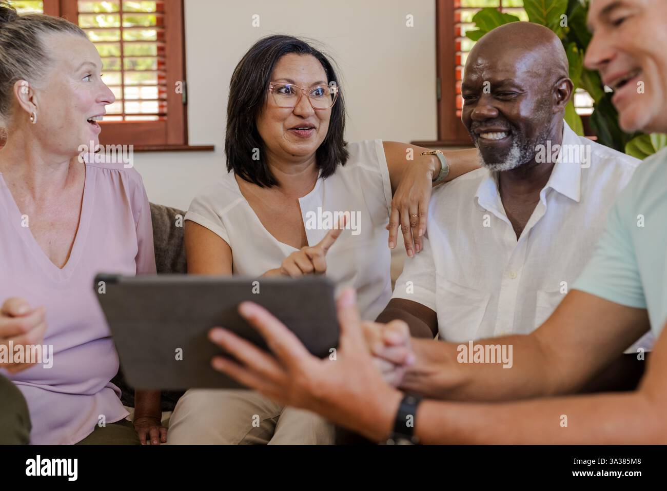 Diverse senior group enjoying conversation while using digital tablet at home Stock Photo