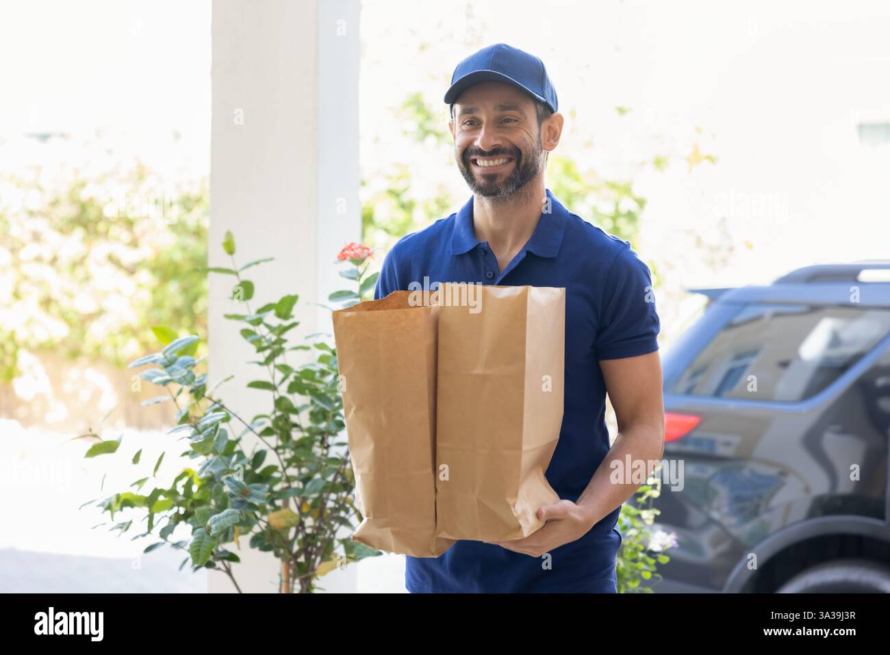 Happy courier man in blue uniform carrying two paper packets, Stock Photo