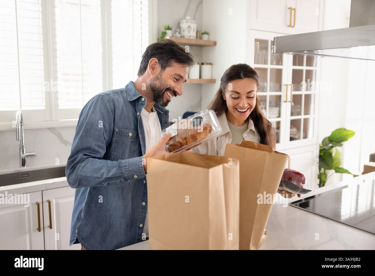 Happy couple unpacking paper supermarket bags with bakery Stock Photo ...
