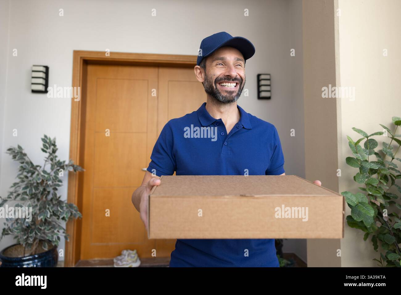 Happy Latin deliveryman in blue uniform carrying parcel Stock Photo