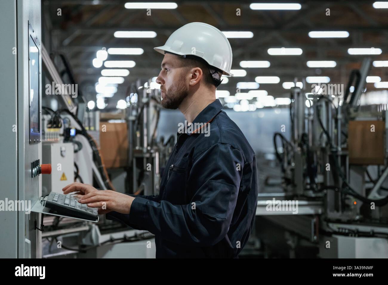 Using equipment, operator. Factory worker is indoors with hard hat. Stock Photo