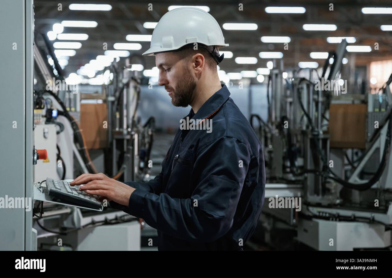 Using equipment, operator. Factory worker is indoors with hard hat. Stock Photo