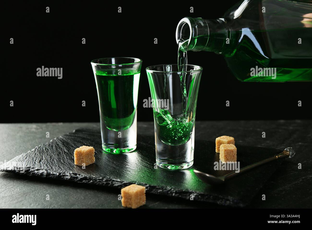 Pouring delicious absinthe from bottle into shot glass at grey textured ...