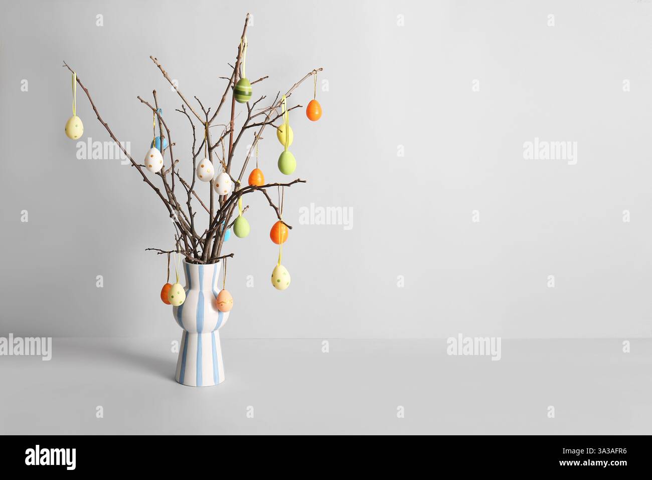 Vase with tree branches and colorful Easter eggs on white background Stock Photo