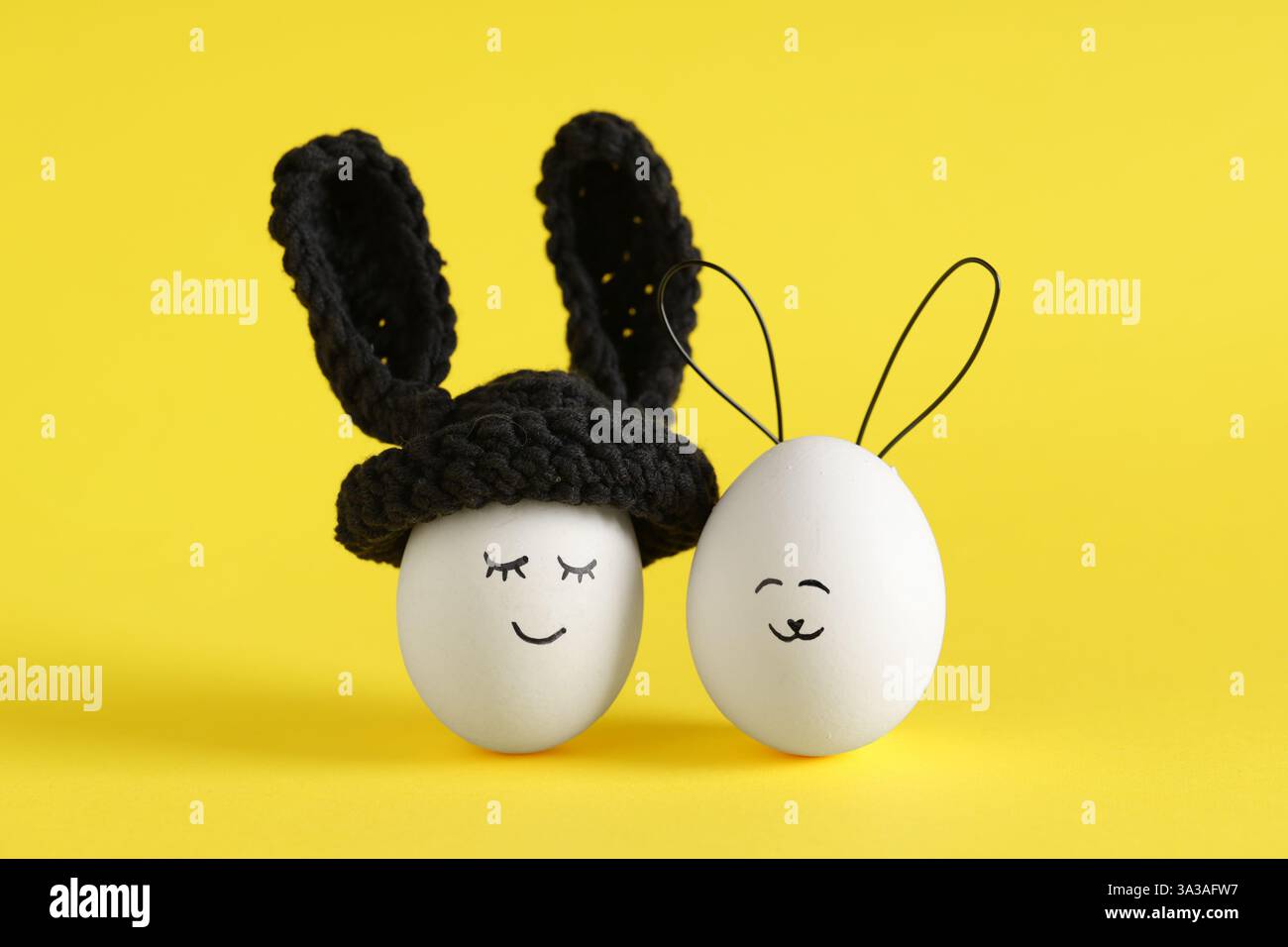Funny Easter eggs with drawn faces in bunny ears on yellow background Stock Photo