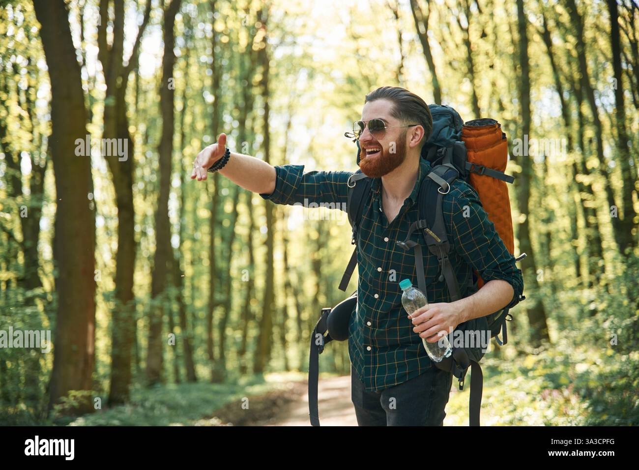 In glasses and with backpack. Bearded man is in the forest at daytime. Stock Photo