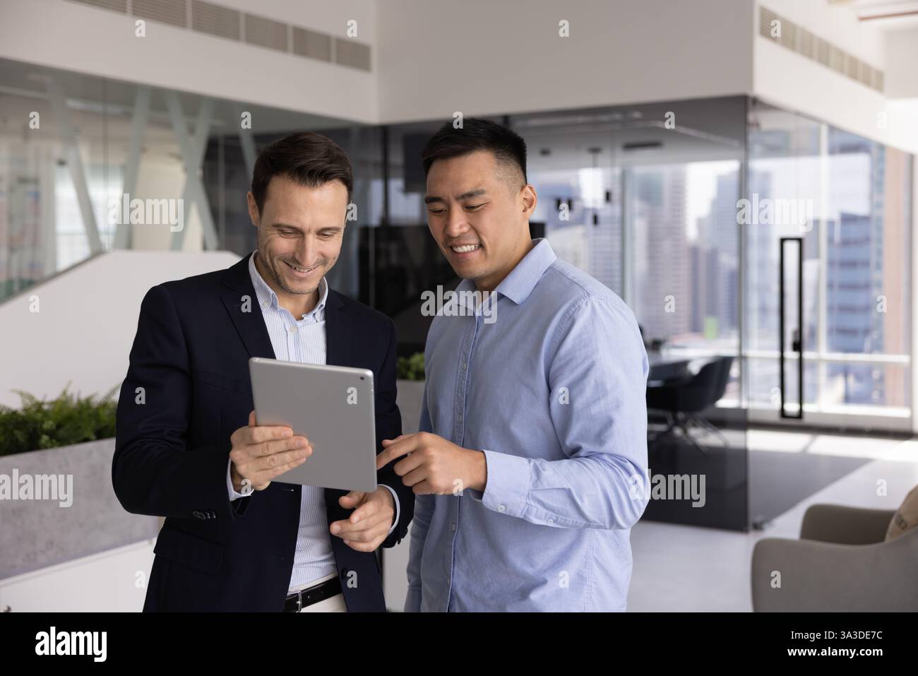 Two positive multiethnic businessmen standing with digital gadget in office Stock Photo