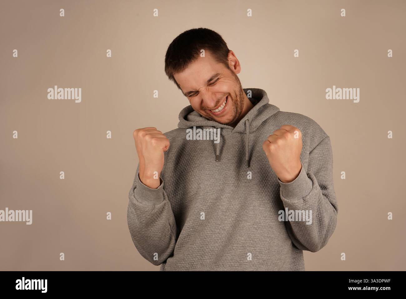 This victorious gesture reflects a moment of success and personal achievement. Ideal for moments of triumph. The man, with a wide grin, lifts his Stock Photo