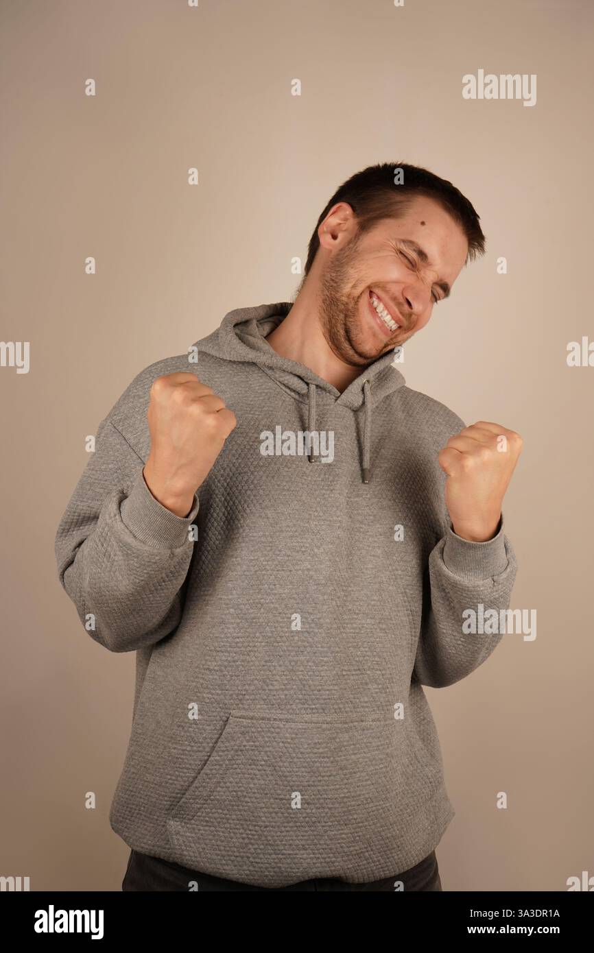 The man, with a wide grin, lifts his fists in celebration, expressing immense joy. This victorious gesture reflects a moment of success and personal Stock Photo