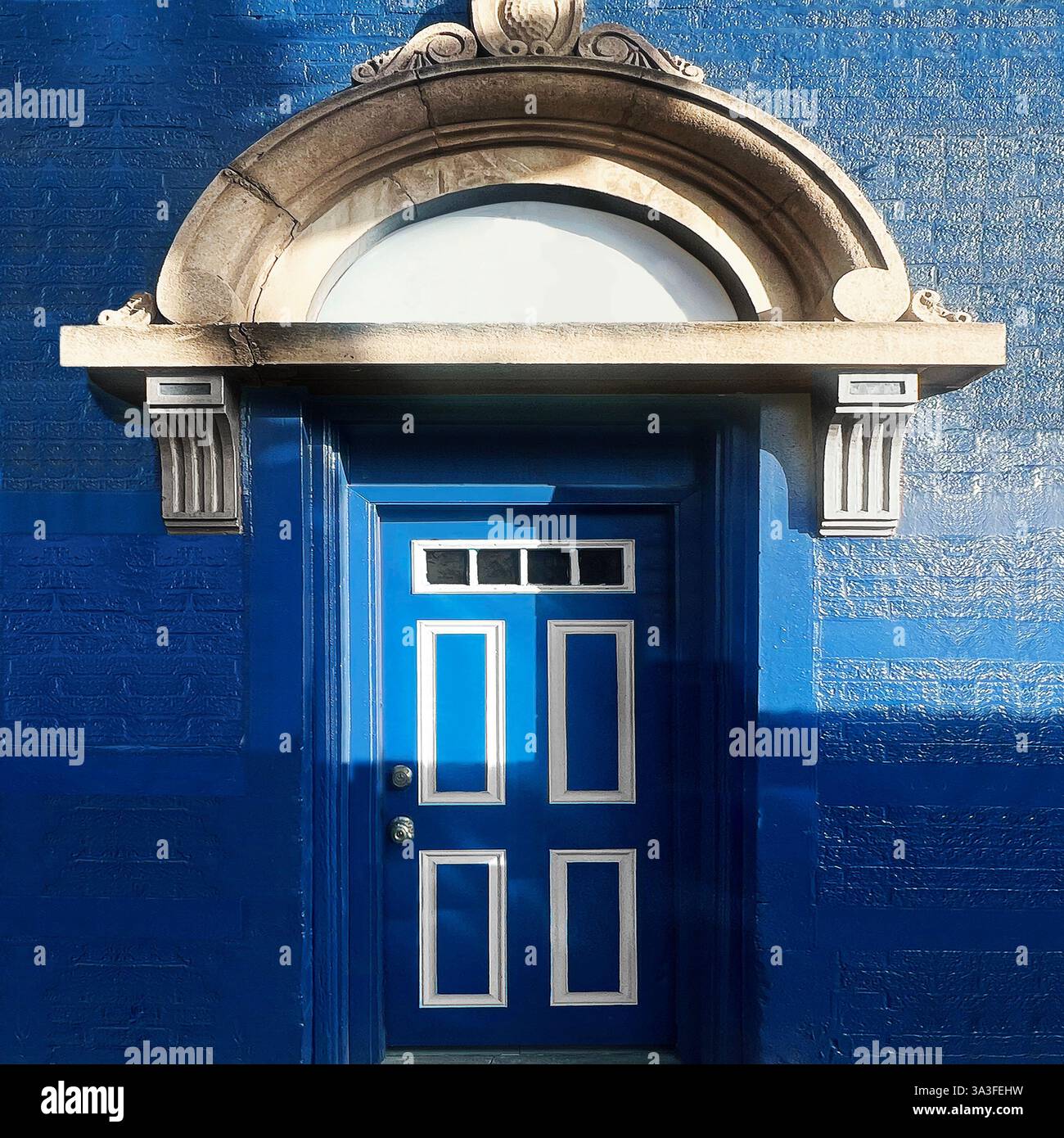 Striking blue door with white accents set within an ornate stone archway, featuring intricate architectural details on a textured blue brick facade. - Smartphone Captured Stock Image