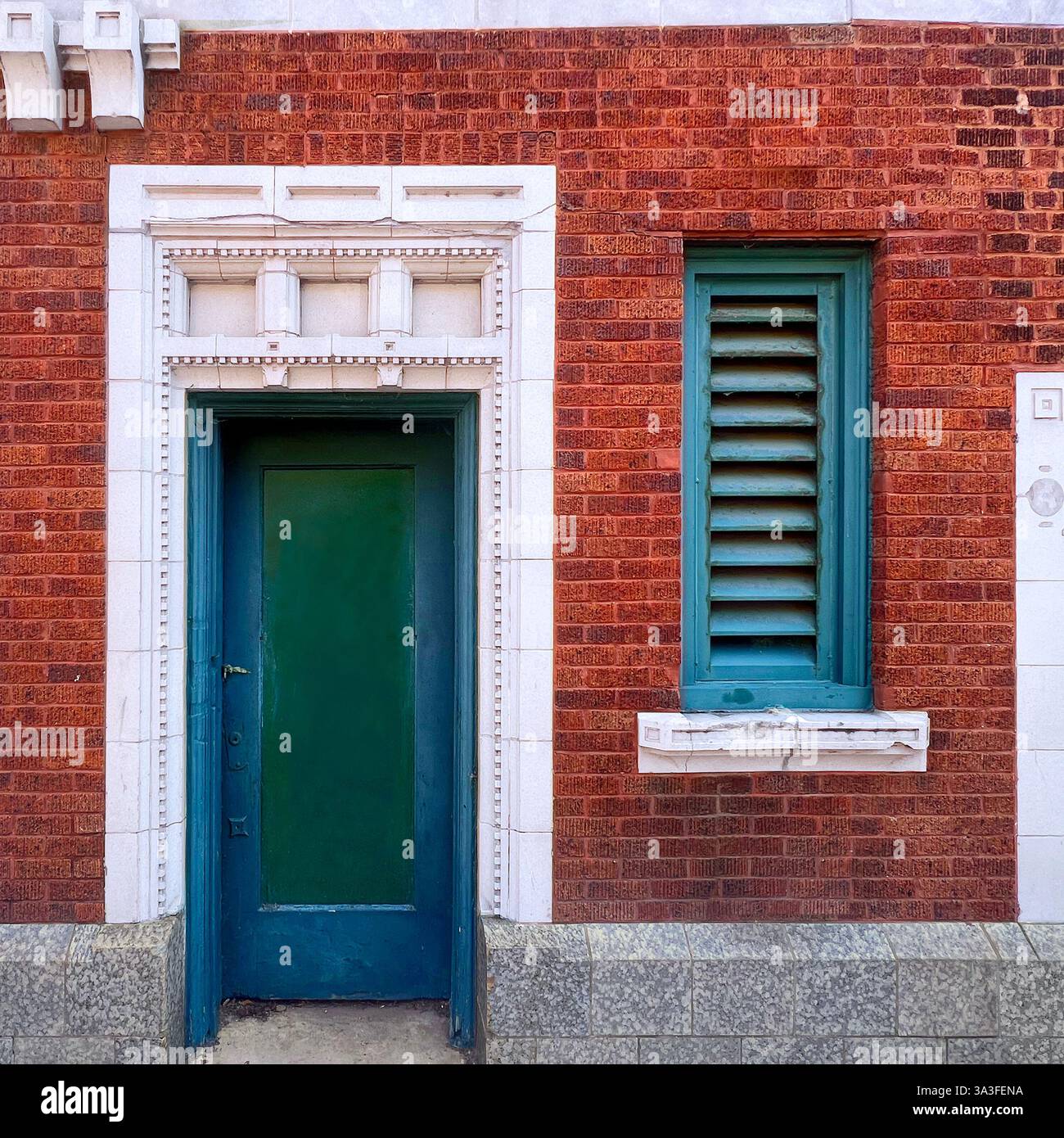 Vintage green door and louvered window set within a historic red brick facade, framed by ornate white stone detailing. - Smartphone Captured Stock Image