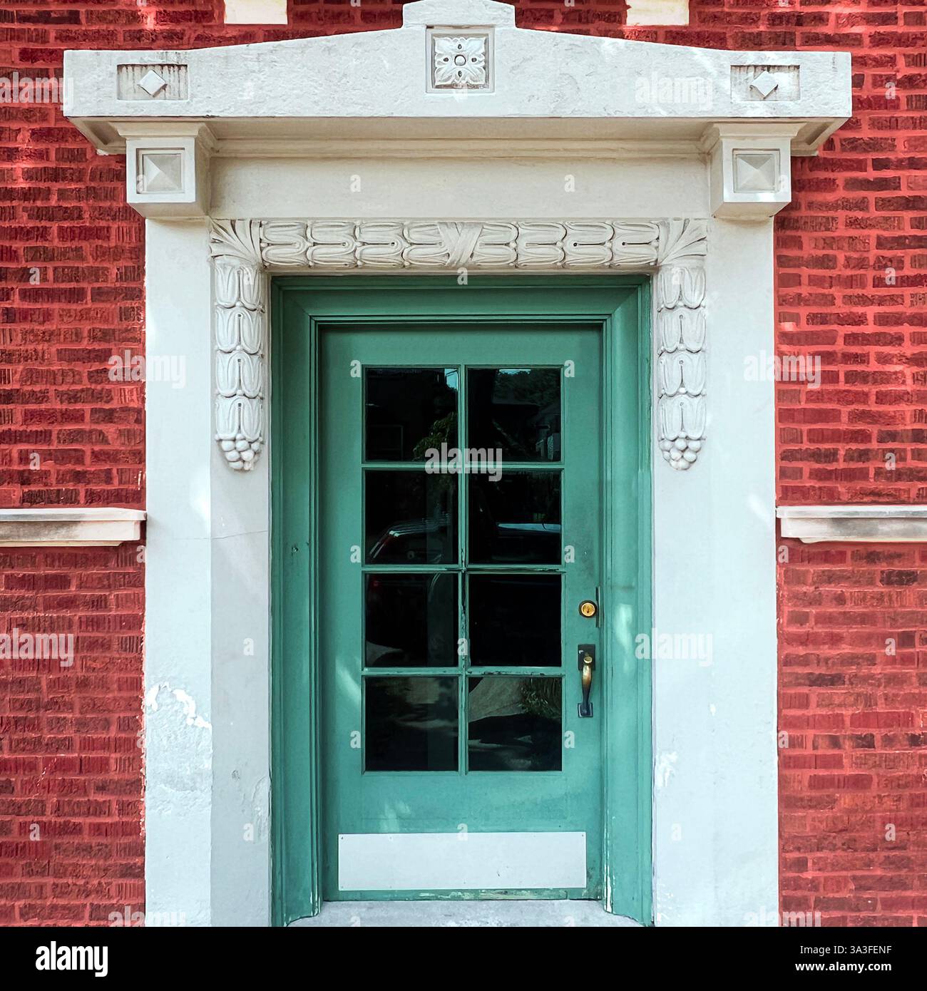 Elegant green glass-paneled door within a historic red brick facade, framed by intricate white stone carvings. - Smartphone Captured Stock Image