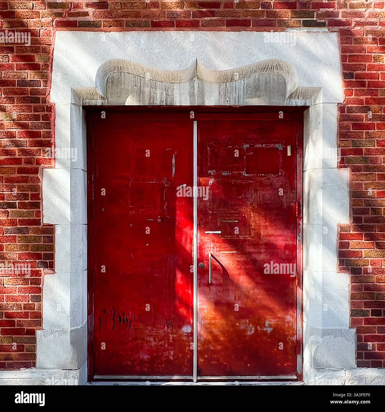 Weathered red double doors set within a historic red brick facade, framed by an ornate white stone archway with sculpted details. - Smartphone Captured Stock Image