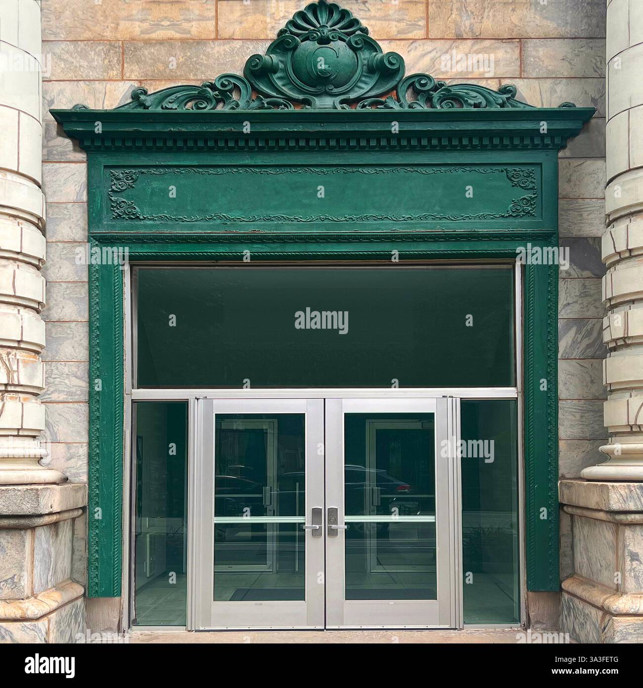 Elegant entrance with silver double glass doors framed by a richly decorated green cast-iron architrave, set within a historic stone facade. - Smartphone Captured Stock Image