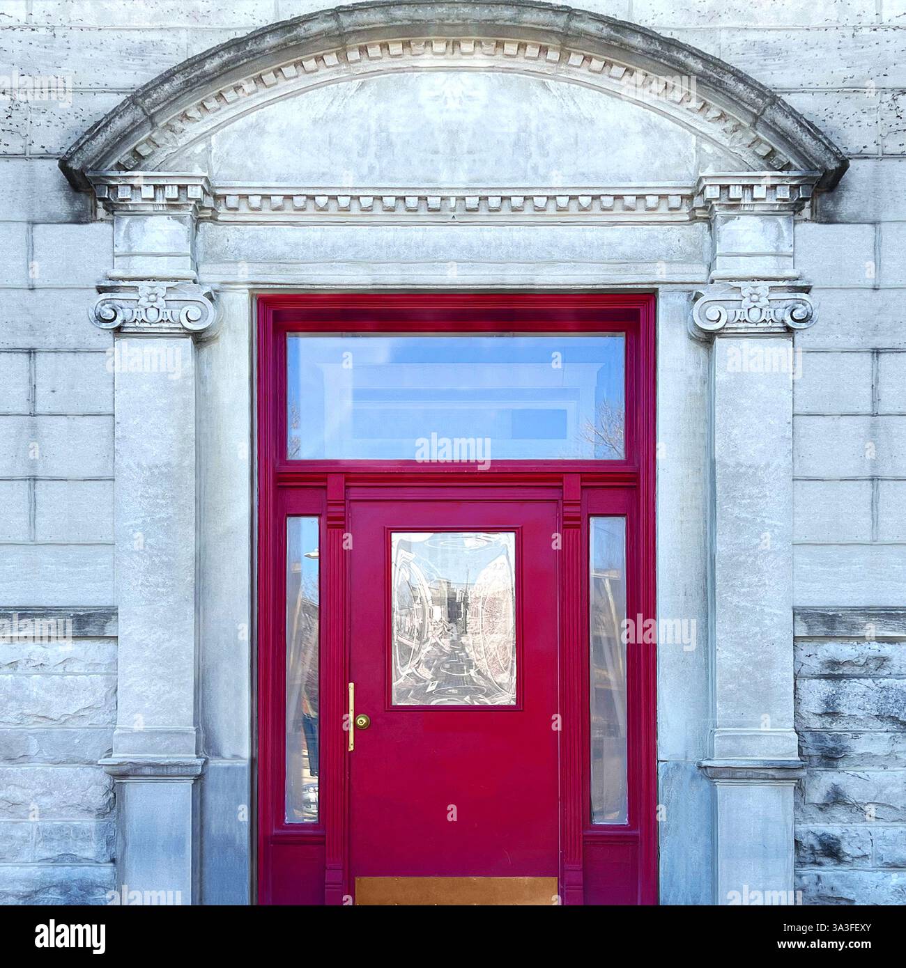 Red doorway with glass panels surrounded by intricate stone detailing and arched pediment, highlighted by symmetrical columns. - Smartphone Captured Stock Image