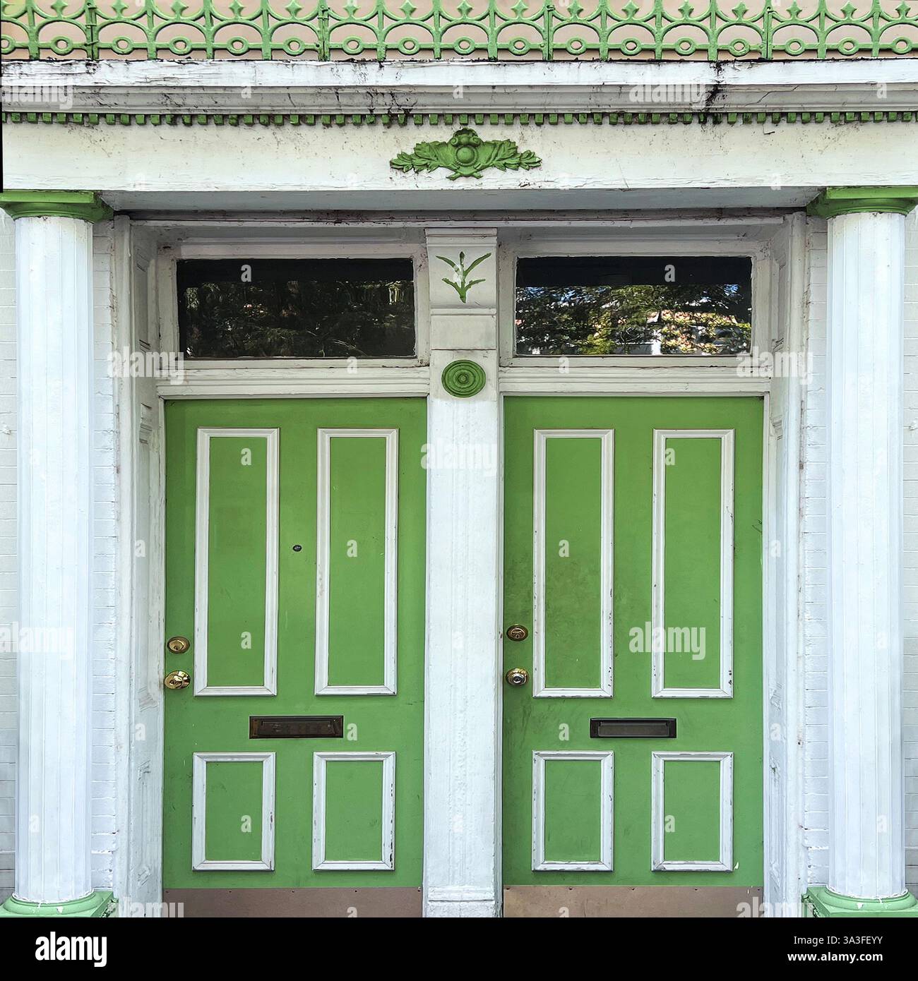 A historic building entrance with double green doors, white columns, and intricate architectural details, featuring molding and decorative railing. - Smartphone Captured Stock Image