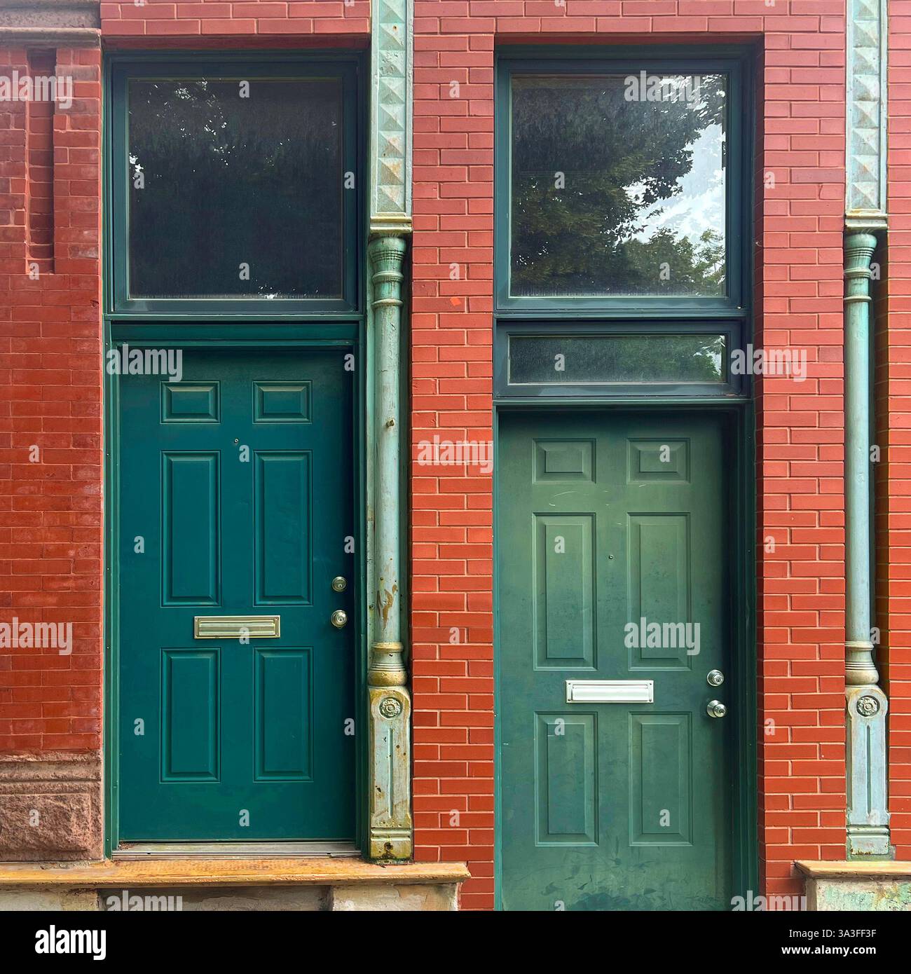 Two contrasting green doors set in a red brick facade, framed by decorative metal columns.. - Smartphone Captured Stock Image