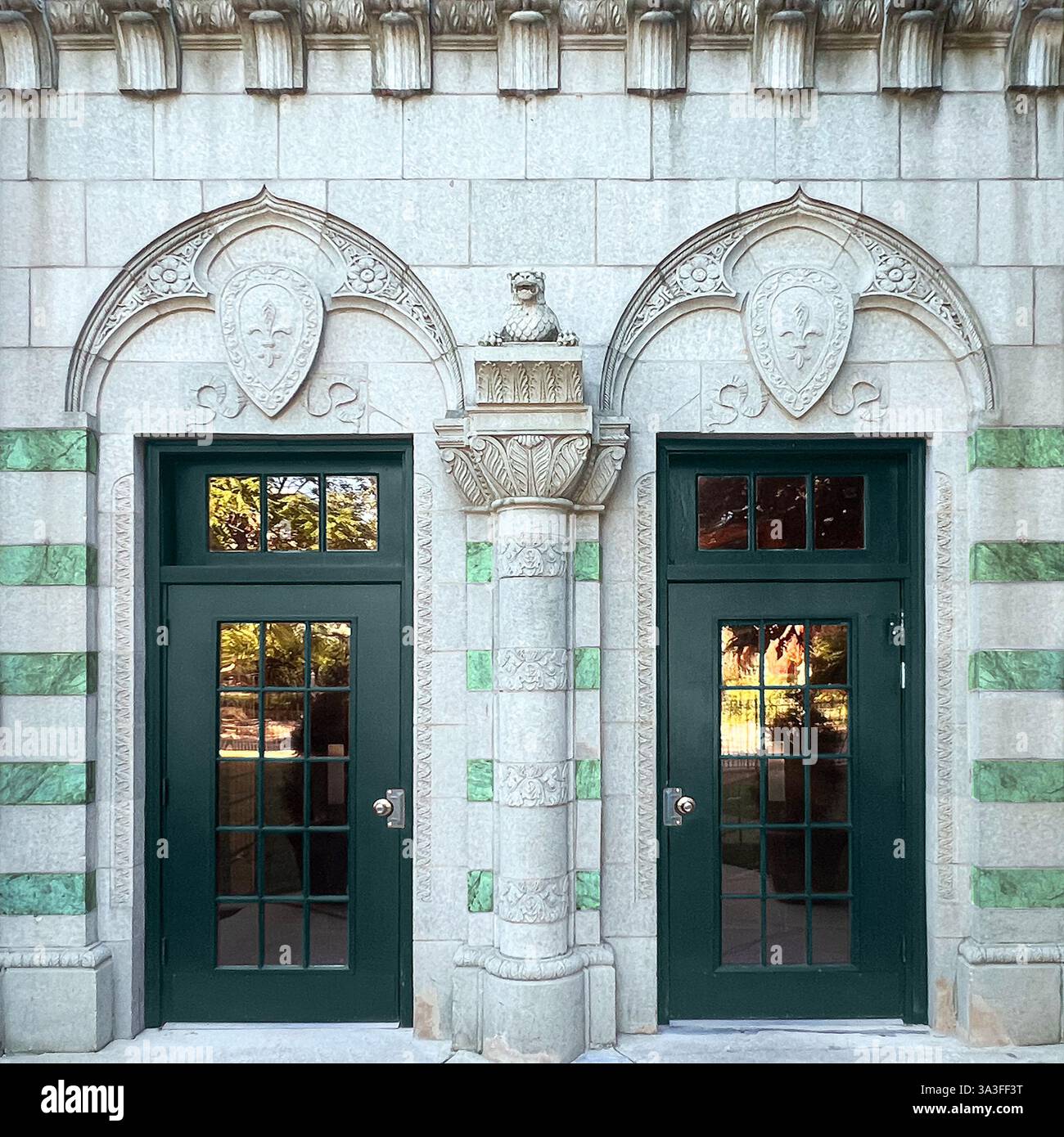 Elegant green double doors with intricate stone carvings, arched shields, and a central decorative column. - Smartphone Captured Stock Image