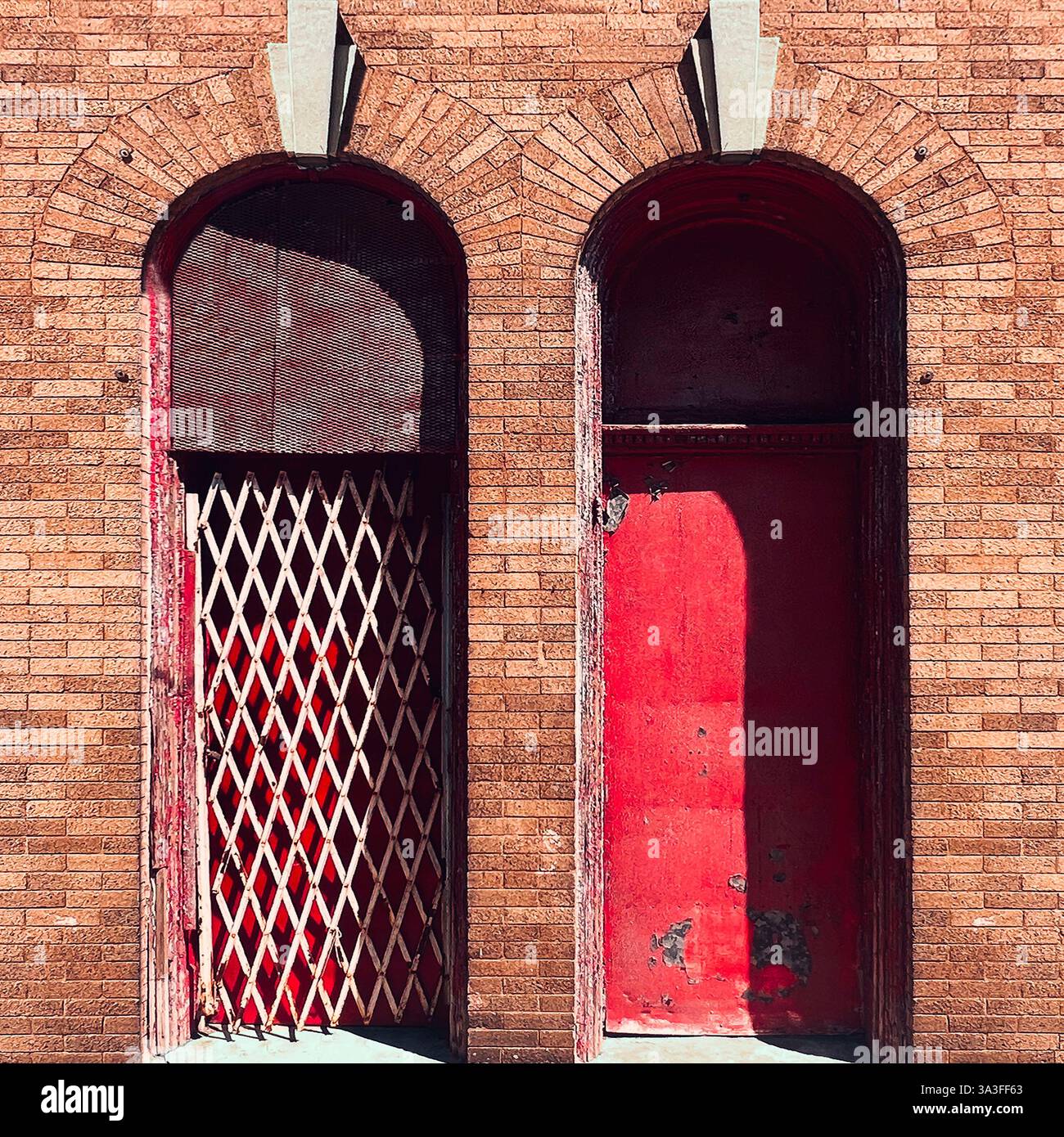 Aged red arched doorways with a metal security gate, surrounded by a warm-toned brick facade, showcasing urban decay and historic architecture. - Smartphone Captured Stock Image