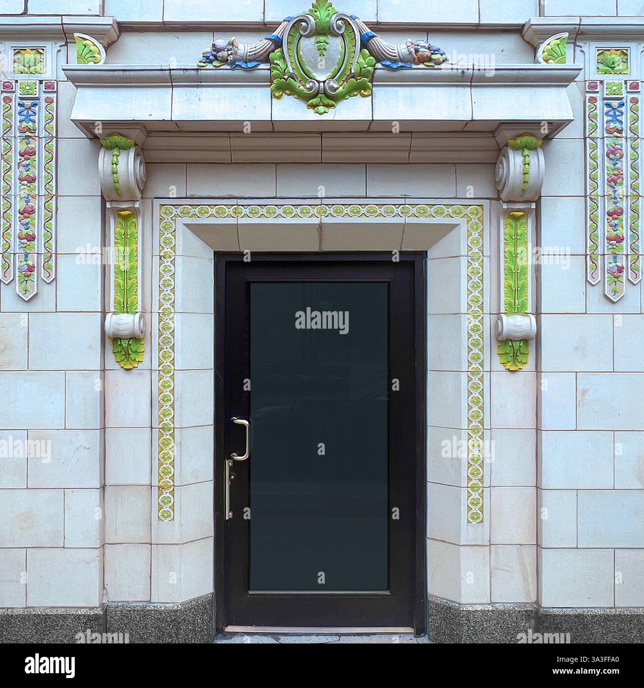 An ornate entrance  framed by decorative glazed terracotta tiles with floral and scroll motifs in green, blue, cream. - Smartphone Captured Stock Image