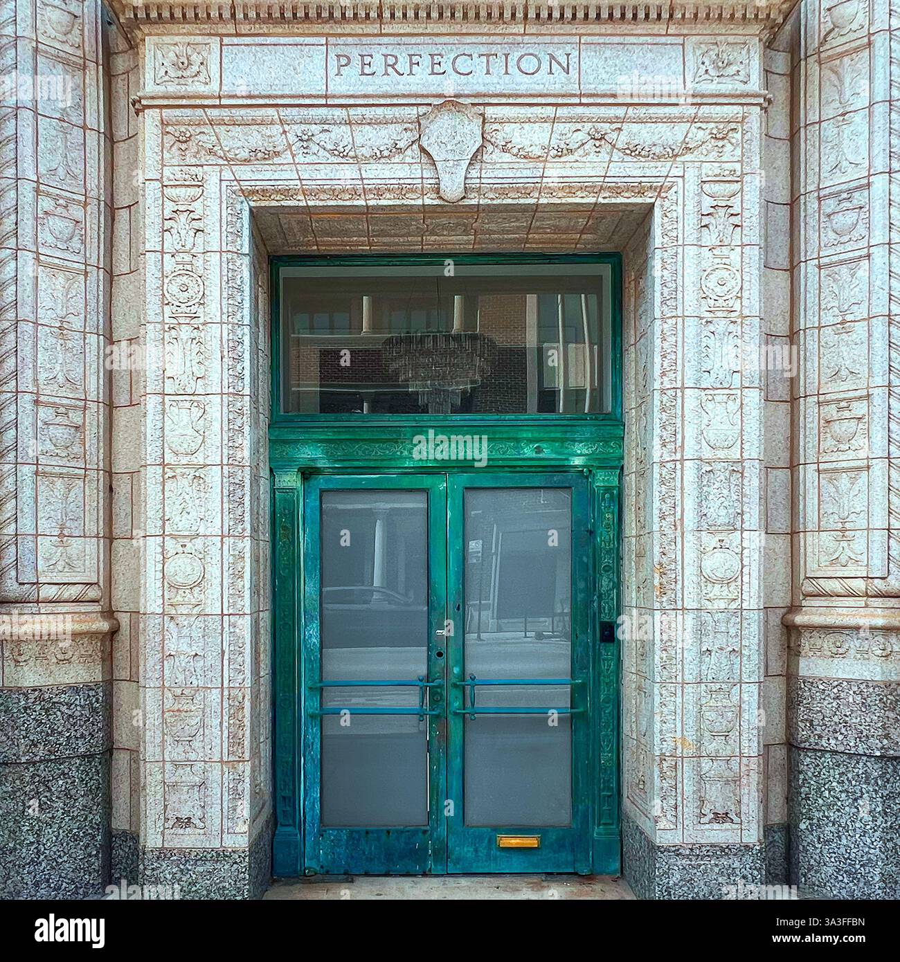 An ornate green double door with a weathered patina, set within an intricately carved stone facade labeled 'PERFECTION,' in Chicago - Smartphone Captured Stock Image