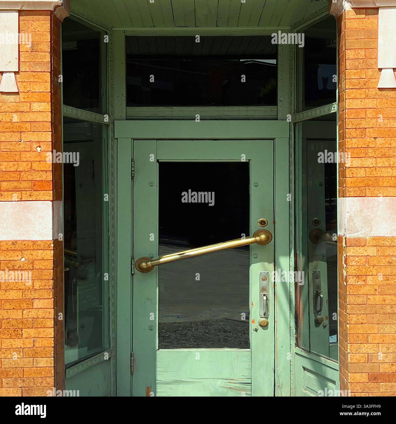 A vintage mint-green entrance withlarge  brass handle, set against a warm-toned brick facade. - Smartphone Captured Stock Image