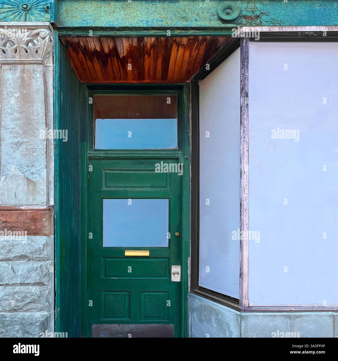 A vintage green storefront with large glass windows reflects the surrounding historic buildings and sky in a Chicago neighborhood - Smartphone Captured Stock Image