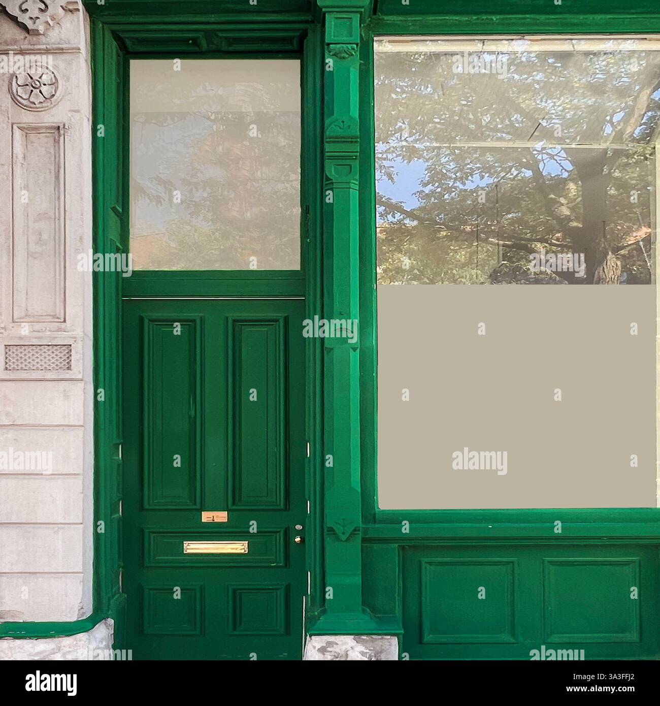 A vintage green storefront with large glass windows reflects the surrounding historic buildings and sky in a Chicago neighborhood. - Smartphone Captured Stock Image