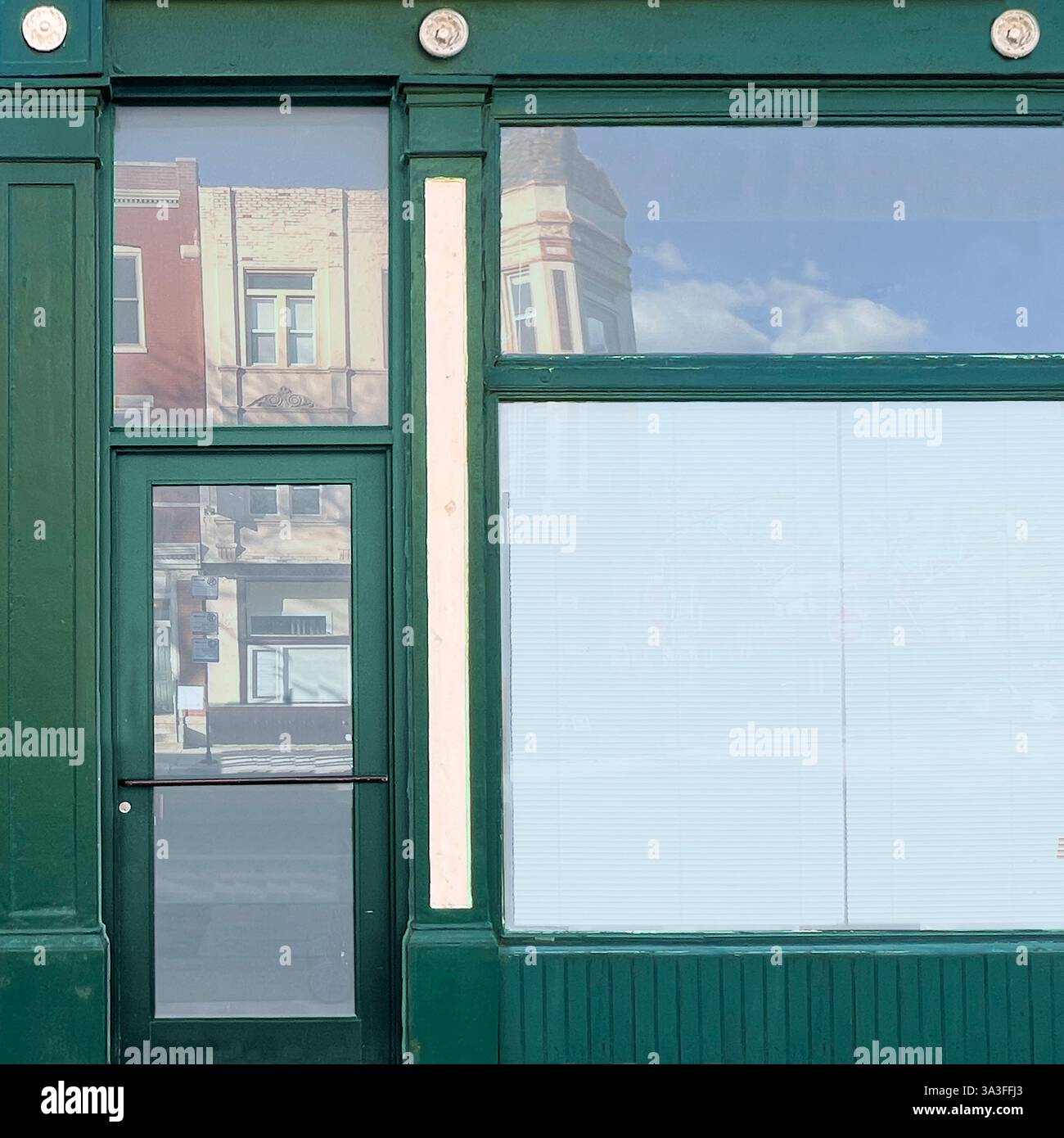 A vintage green storefront with large glass windows reflects the surrounding historic buildings and sky in a Chicago neighborhood. - Smartphone Captured Stock Image