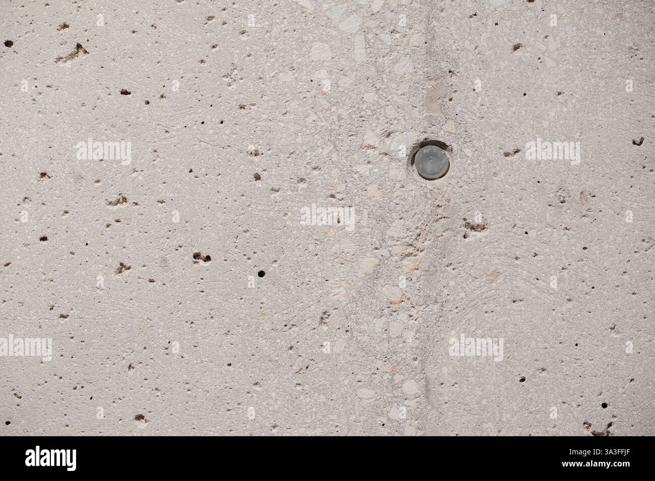 Concrete Wall Texture: Macro shot of a textured concrete surface with an embedded metal disc showcasing its rough and varied patterns Stock Photo