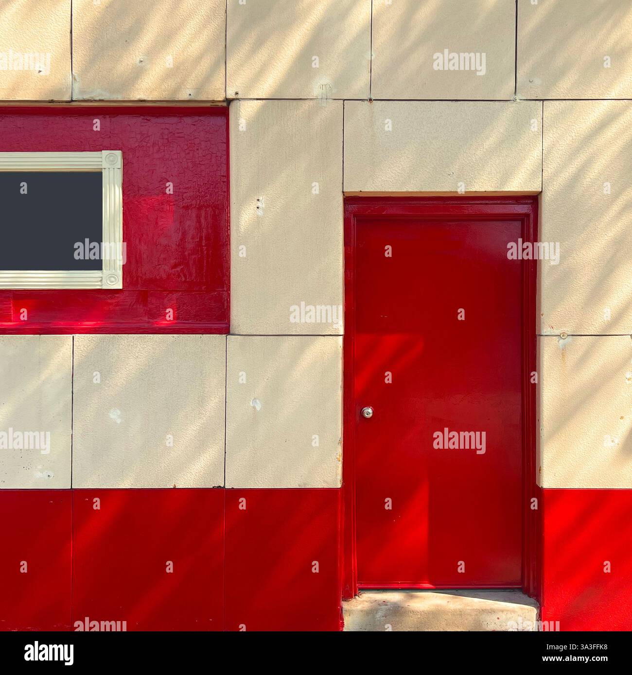 Mimalist facade featuring a bold red door and matching red window panel, framed by textured yellow tiles. - Smartphone Captured Stock Image