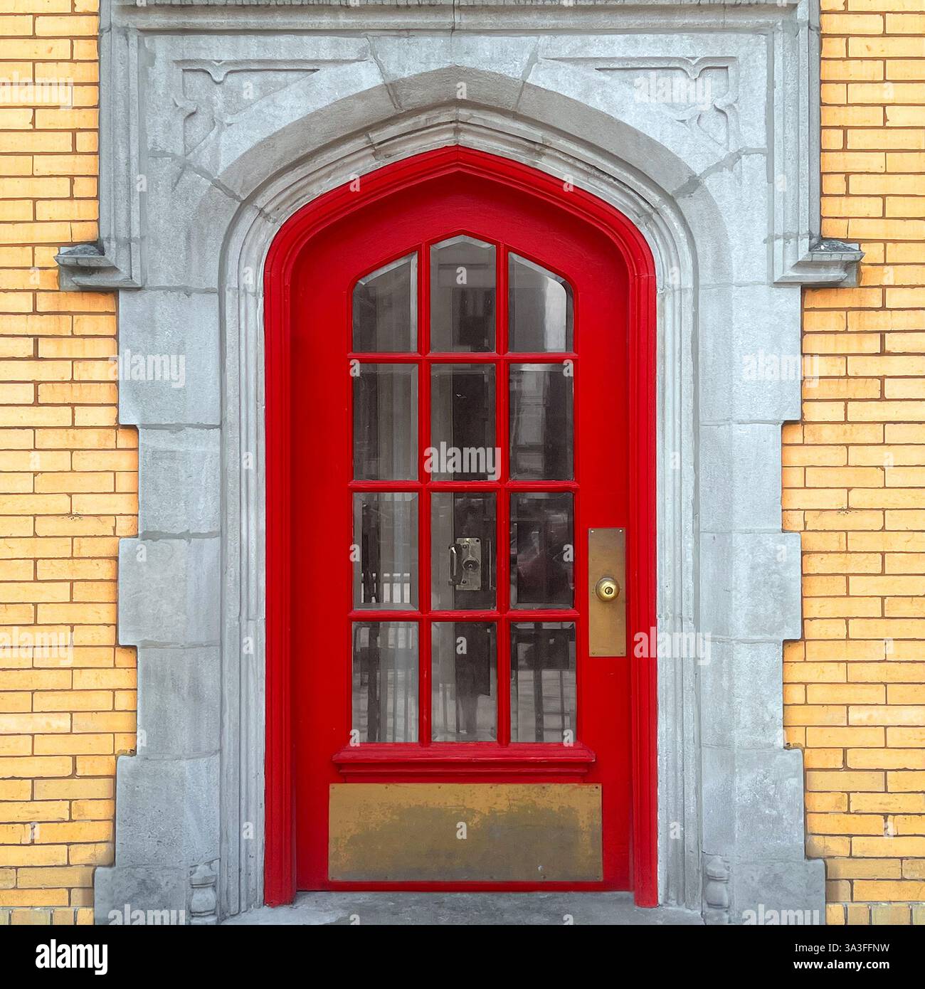 Gothic-style red arched doorway with glass panes set within a historic stone and yellow brick facade. - Smartphone Captured Stock Image
