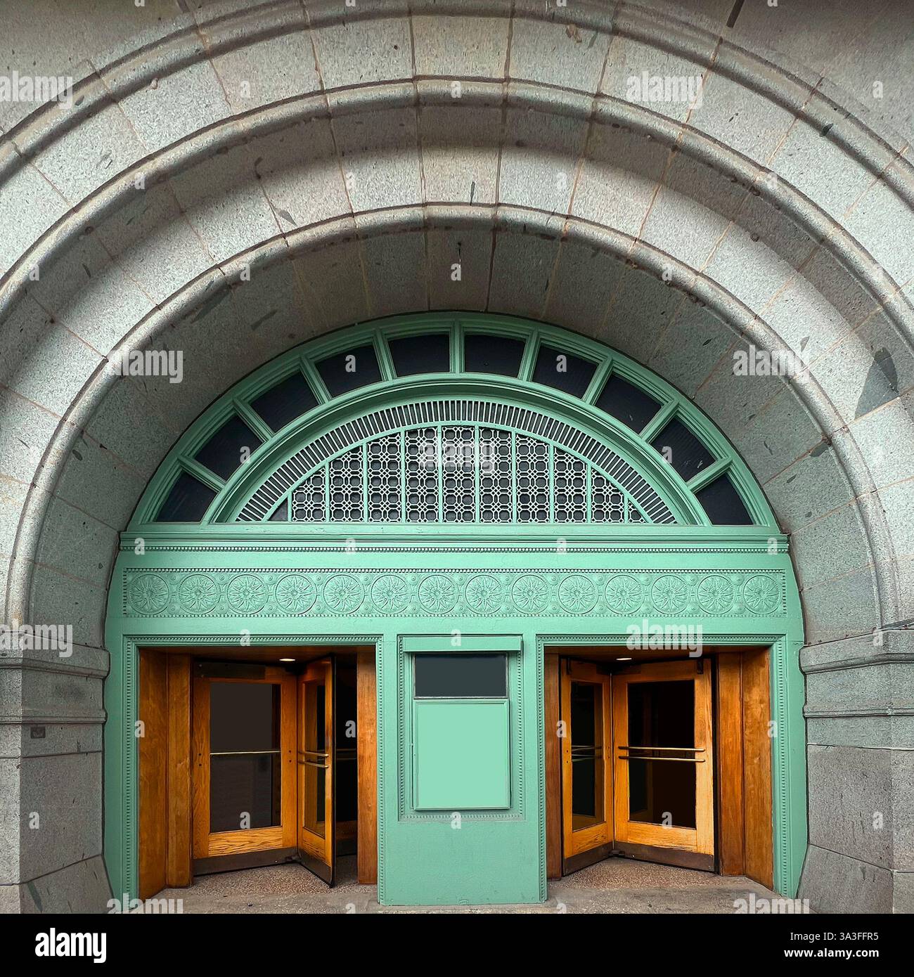 Historic arched entrance with intricate mint green detailing and wooden revolving doors, set within a stone facade. - Smartphone Captured Stock Image