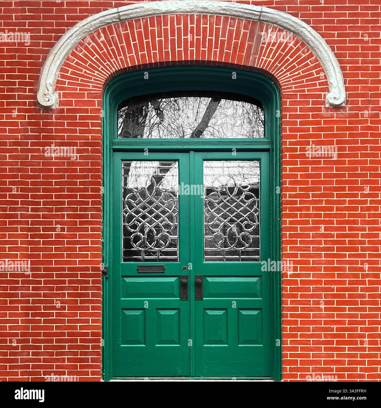 Elegant green double doors with intricate glasswork set within a historic red brick facade. - Smartphone Captured Stock Image
